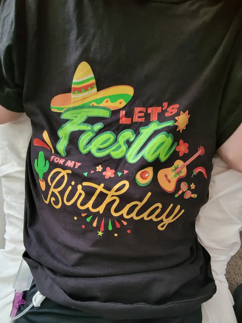 A festive shirt with a sombrero, cactus, guitar, and maracas that says "Let's Fiesta for my Birthday".