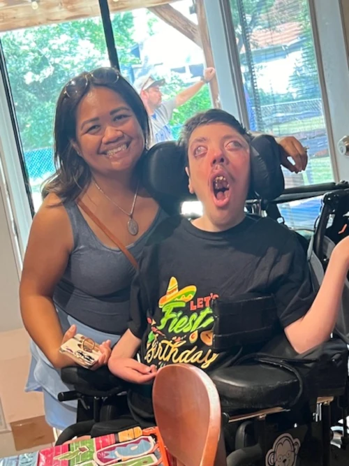 A woman smiling and standing next to a boy in a wheelchair.