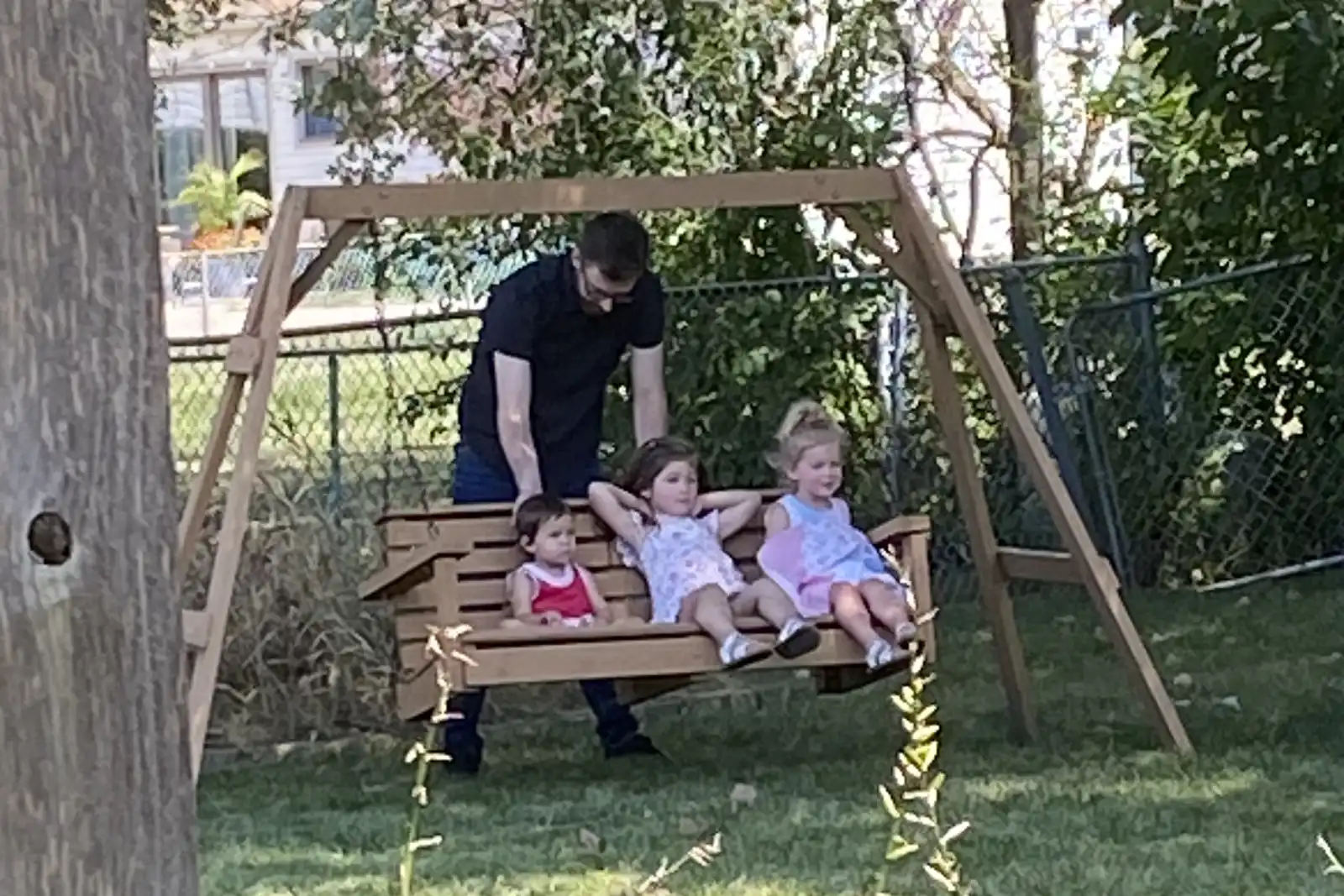 Three small children on a wooden a-frame swing being pushed by a man