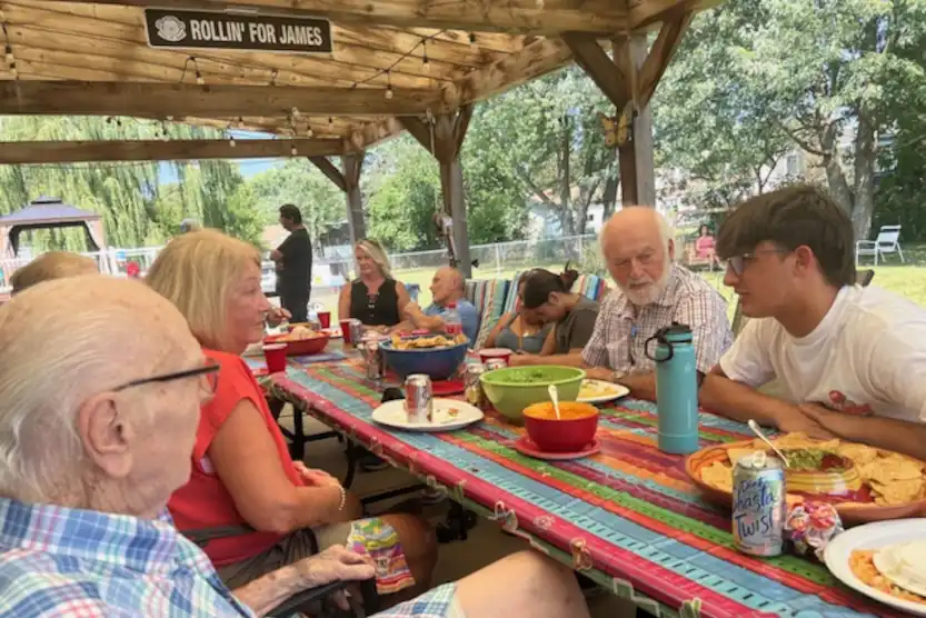 Friends and family sitting at a long table outside enjoying food and conversation.